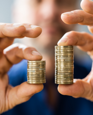 Eine Person hält zwei unterschiedlich hohe Münzstapel. Sie veranschaulichen Gehaltsunterschiede, die durch die EU-Entgelttransparenzrichtlinie sichtbarer werden sollen.