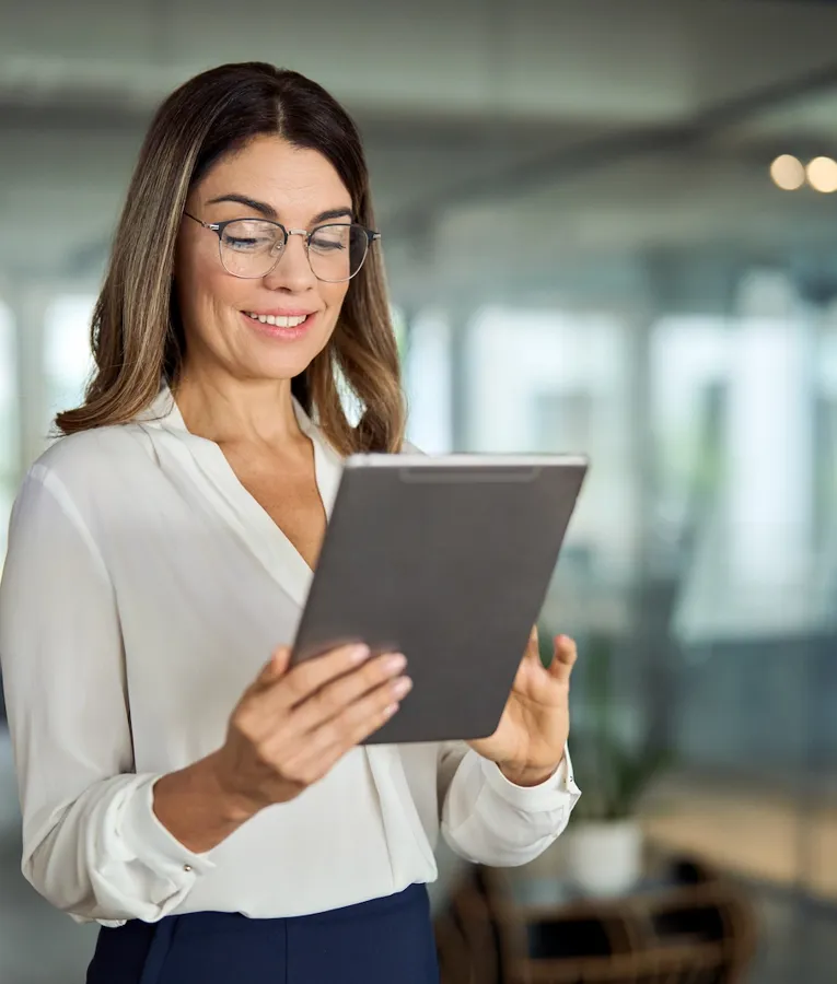 Eine fröhliche Geschäftsfrau in weißer Bluse sitzt an ihrem Schreibtisch, telefoniert und arbeitet an ihrem Laptop. Das Bild symbolisiert Produktivität, Kommunikation und effizientes Workforce Management.