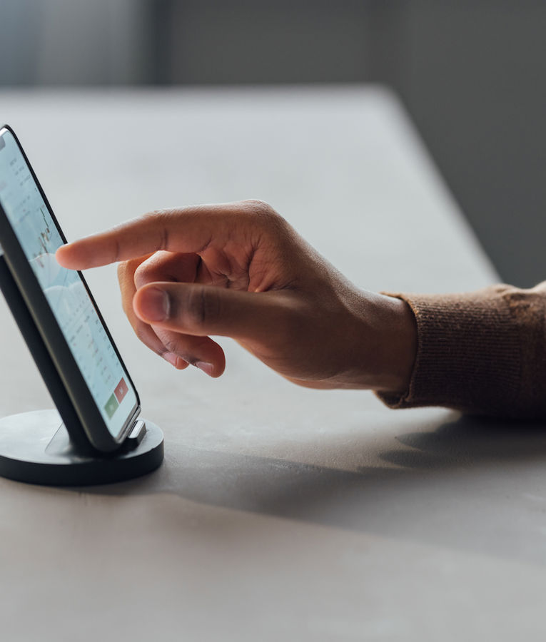 Nahaufnahme einer Person, die ein Smartphone in einer Halterung nutzt und mit einer Finanz- oder Datenanalyse-App interagiert – auf dem Display sind Diagramme und Grafiken zu sehen. Ideal für Inhalte rund um mobiles Workforce Management, Produktivitäts-Apps oder digitale Business-Tools.