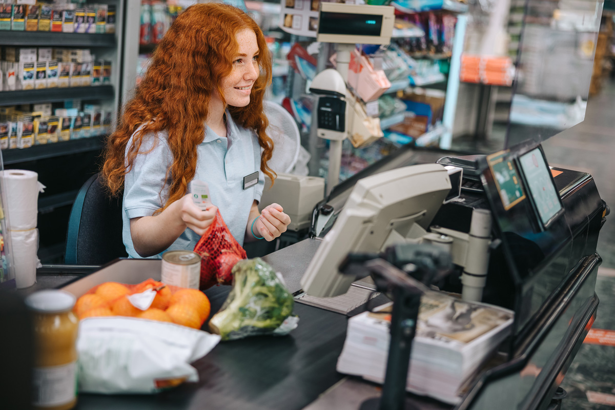 Eine Kassiererin bzw. ein Kassierer in einem Supermarkt scannt die Waren und unterstützt die Kundschaft, um ein schnelles und reibungsloses Einkaufserlebnis zu gewährleisten.