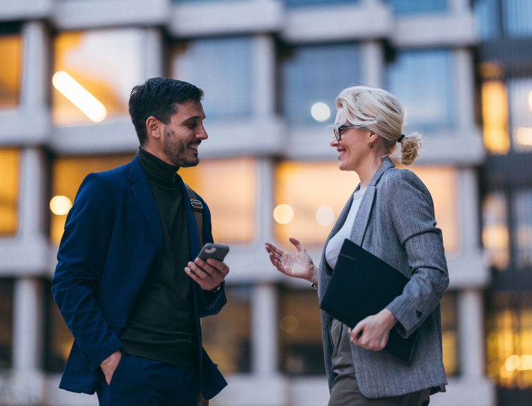 Zwei Kolleginnen bzw. Kollegen in einem geschäftlichen Umfeld besprechen Themen wie Workforce Management, Dienstplanung und Zeiterfassung unter Einsatz eines mobilen Endgeräts.