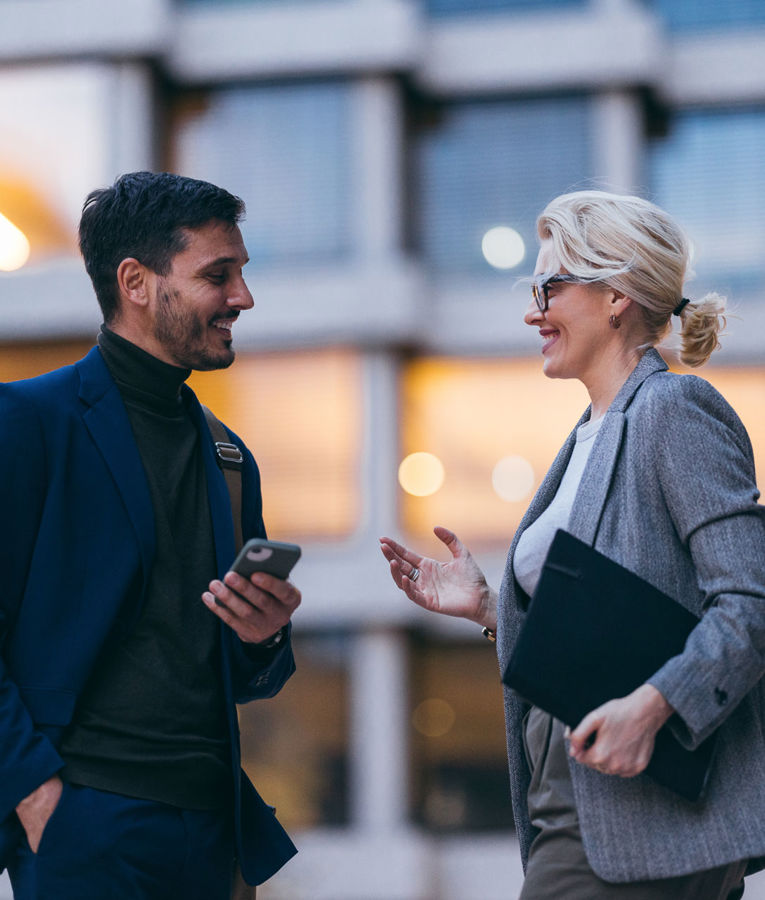 Zwei Kolleginnen bzw. Kollegen in einem geschäftlichen Umfeld besprechen Themen wie Workforce Management, Dienstplanung und Zeiterfassung unter Einsatz eines mobilen Endgeräts.