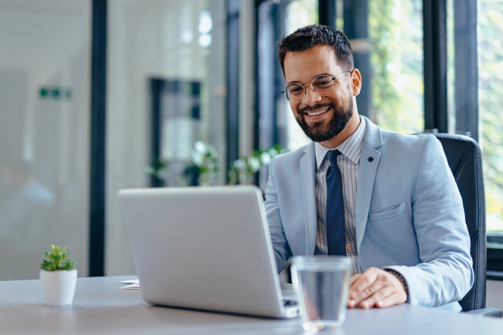 Lächelnder Geschäftsmann in einem modernen Büro arbeitet an einem Laptop und steuert Workforce-Prozesse sowie Geschäftsstrategien, ein Symbol für digitale Produktivität und Führungsstärke.